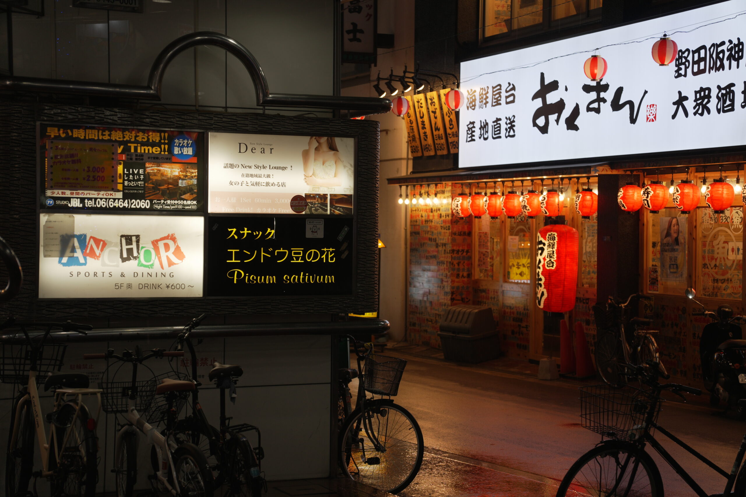 Red lanterns outside an Okuman restaurant, illuminated bar signs and bicycles near Torikizoku in Noda-Hanshin